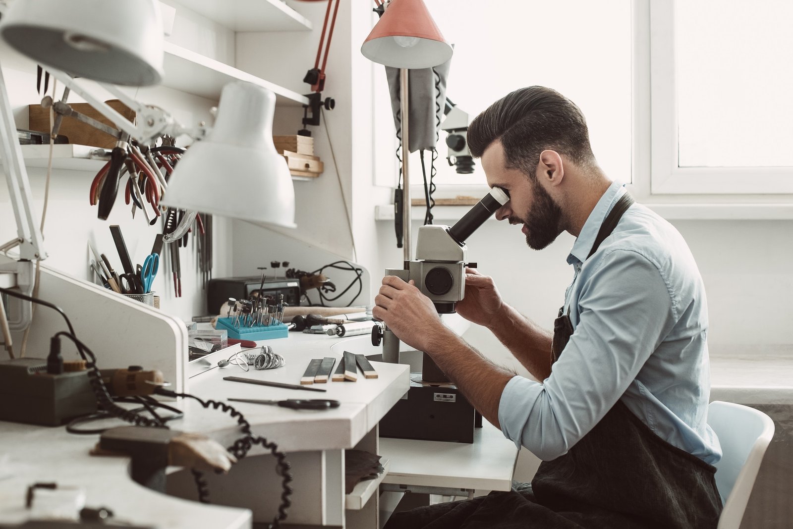 Very close. Side view of a male jeweler looking at the new jewelery product through microscope in a